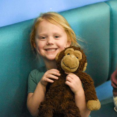 Child holding a plush monkey toy at wake orthodontics & pediatric dentistry, representing the safety of laser dentistry for kids